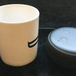 An Amazon Echo Dot smart speaker beside a mug