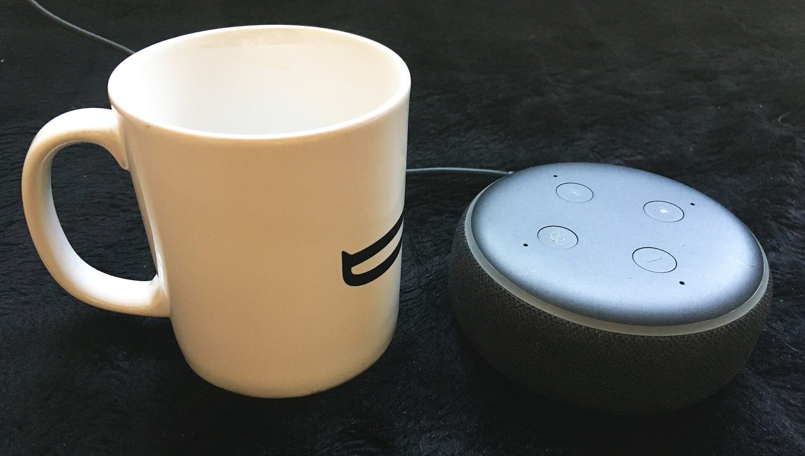 An Amazon Echo Dot smart speaker beside a mug